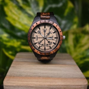 May include: A wooden wristwatch with a black face and brown wooden band. The face features a compass design with runes around the edge.