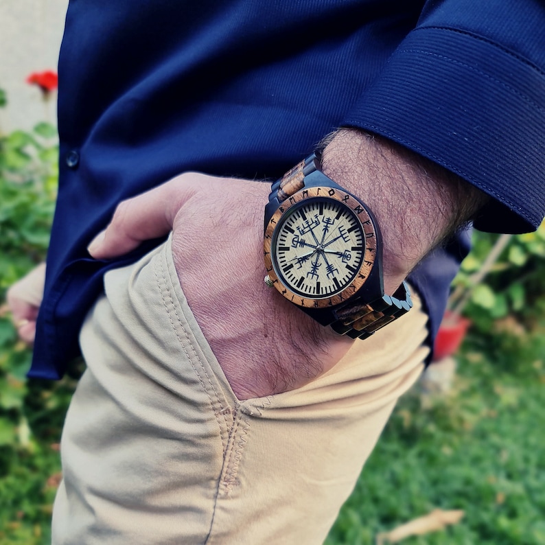 May include: A wooden wristwatch with a black and brown band. The watch face features a compass design with runes around the edge.