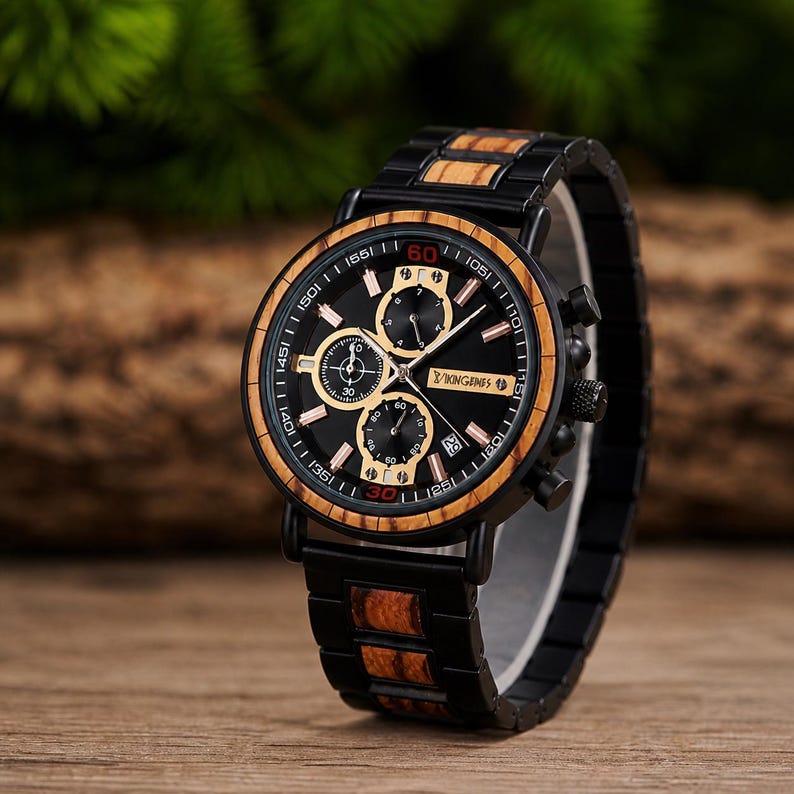 Puede incluir: Un reloj de pulsera negro con bisel y correa de madera. La esfera del reloj es negra con detalles dorados y tres subesferas. El reloj tiene el texto "KINGINFS" en la esfera. El reloj se muestra sobre una superficie de madera.