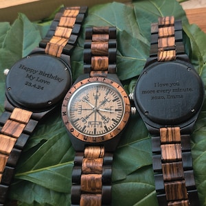 May include: Three wooden wristwatches with black faces. The watch on the left has the inscription "Happy Birthday My Love 23.4.24". The watch in the middle has a compass face with runes around the edge. The watch on the right has the inscription "I love you more every minute. xoxo, Emma".