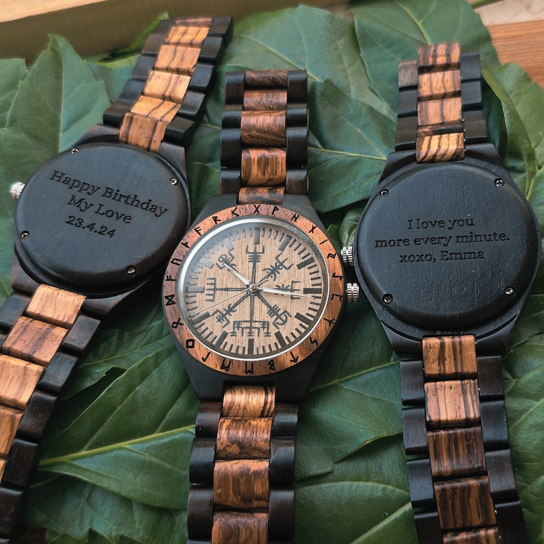 May include: Three wooden wristwatches with black faces. The watch on the left has the inscription "Happy Birthday My Love 23.4.24". The watch in the middle has a compass face with runes around the edge. The watch on the right has the inscription "I love you more every minute. xoxo, Emma".