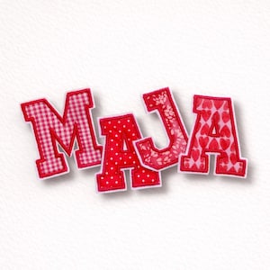 Könnte beinhalten: Rote Stoffbuchstaben mit weißem Rand, die "MAJA" buchstabieren. Das "M" hat ein rot-weißes Vichy-Muster, das "A" hat ein rotes Tupfenmuster, das "J" hat ein Blumenmuster und das letzte "A" hat ein Herzmuster.
