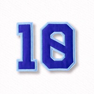 Könnte beinhalten: Zwei blaue Stoffnummern-Patches mit der Zahl "18". Die Zahlen sind tiefblau mit einem hellblauen Rand. Diese Patches eignen sich für Kleidung oder Bastelprojekte.
