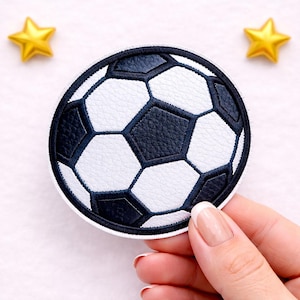 Könnte beinhalten: Ein runder Aufnäher mit einem Fußball-Design. Der Ball hat ein klassisches schwarz-weißes Muster mit strukturierter Oberfläche. Zwei goldene sternförmige Verzierungen befinden sich im Hintergrund.