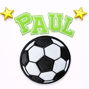 Könnte beinhalten: Ein gestickter Aufnäher mit einem schwarz-weißen Fußball, zentriert unter dem Namen PAUL in lindgrünen Blockbuchstaben mit weißer Umrandung, flankiert von zwei gelben fünfzackigen Sternen links und rechts neben dem Schriftzug.