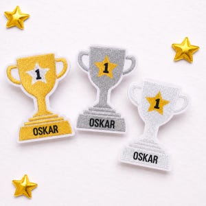 May include: Three embroidered trophy patches with white borders. One gold trophy features a white star with the number 1 and the name OSKAR. Two silver trophies feature yellow stars with the number 1 and the name OSKAR. Three small gold star patches.