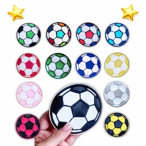 Könnte beinhalten: Eine Sammlung von Fußball-Patches in verschiedenen Farben, darunter Schwarz, Weiß, Rot, Grün, Blau, Rosa und Gelb. Die Patches sind rund mit einem klassischen Fünfeck-Design. Zwei goldfarbene sternförmige Verzierungen sind ebenfalls vorhanden.