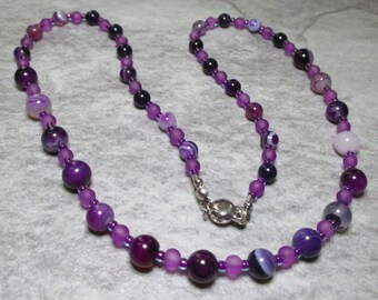 May include: A purple and white agate bead necklace with a silver clasp. The necklace is made of small, round beads and is approximately 18 inches long.