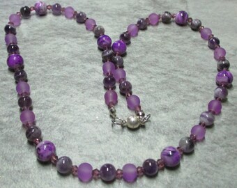 May include: A purple and gray beaded necklace with a silver clasp. The beads are made of glass and amethyst.