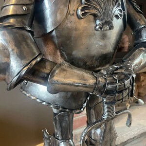 Op de afbeelding: Een zilveren metalen ridderbeeld met een zwaard in zijn hand. De ridder draagt ​​een harnas met een decoratief schelpontwerp op de borst.