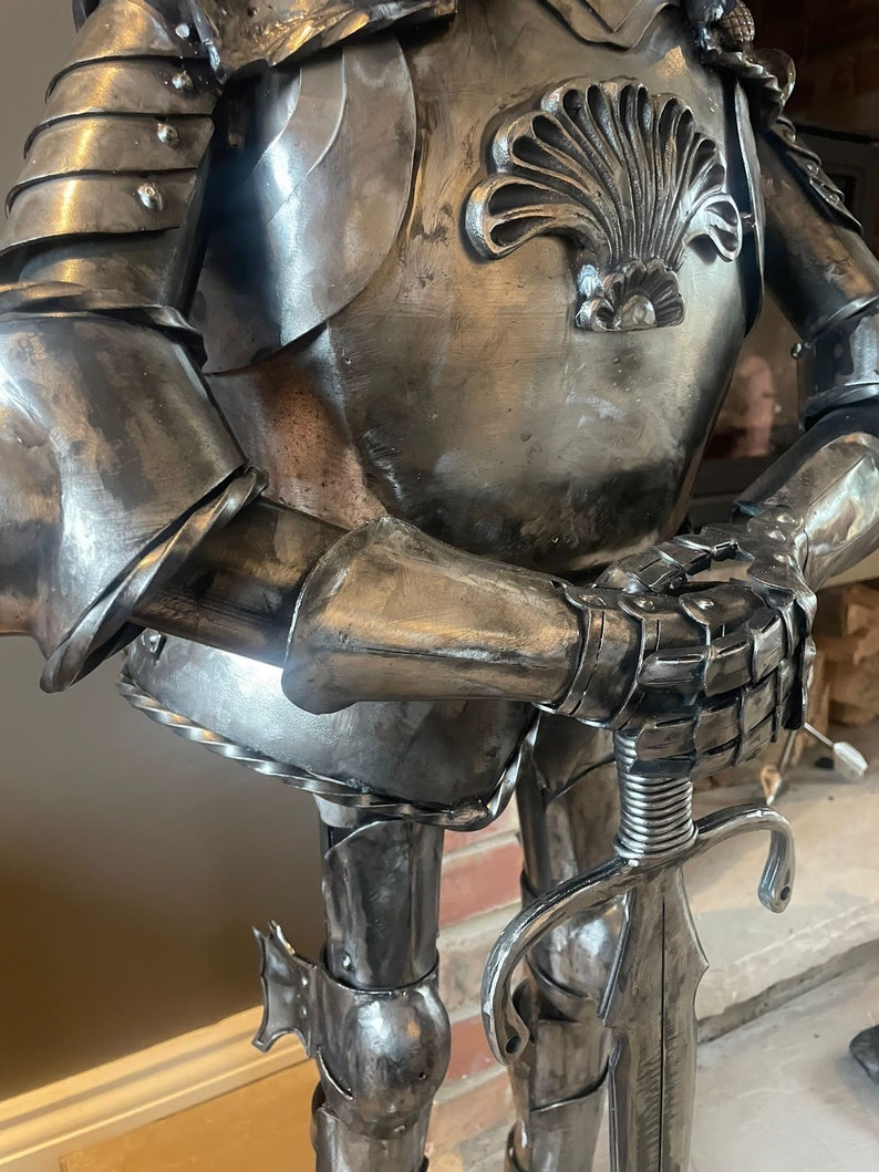 Op de afbeelding: Een zilveren metalen ridderbeeld met een zwaard in zijn hand. De ridder draagt ​​een harnas met een decoratief schelpontwerp op de borst.
