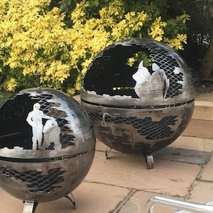 May include: Two metal fire pit spheres with intricate cutouts. One sphere features a Star Wars scene with Luke Skywalker and a character from the movie. The other sphere has a more abstract design.