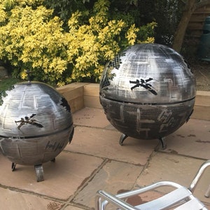 May include: Two metal fire pits shaped like the Death Star from Star Wars. The fire pits are on a patio with chairs.