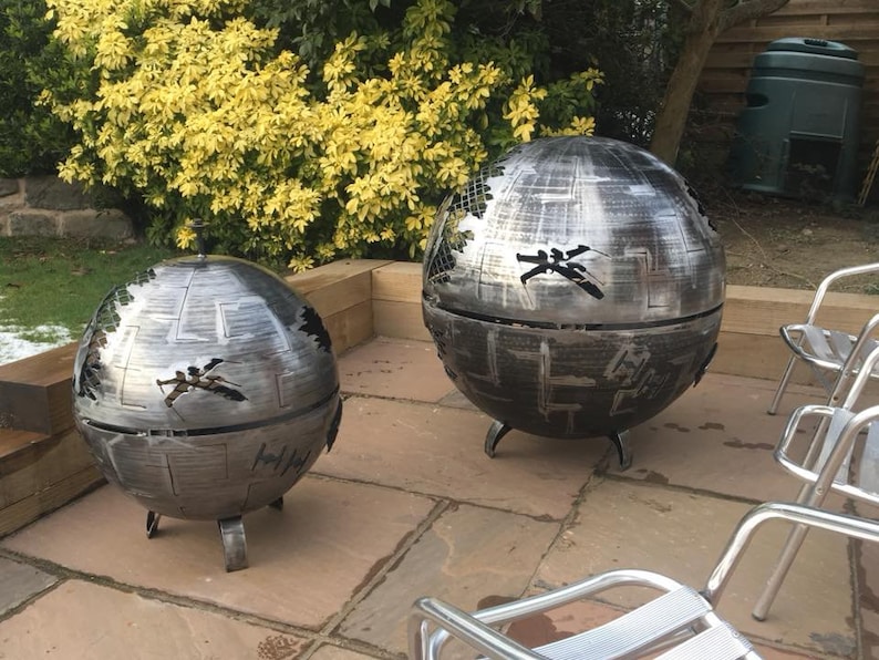 May include: Two metal fire pits shaped like the Death Star from Star Wars. The fire pits are on a patio with chairs.