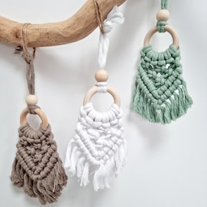 May include: Three macrame wall hangings with wooden rings. The hangings are in brown, white, and green.