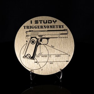May include: A gold-colored round metal disc with the text "I STUDY TRIGGERNOMETRY" and a black and white illustration of a handgun with trigonometric functions labeled around it.