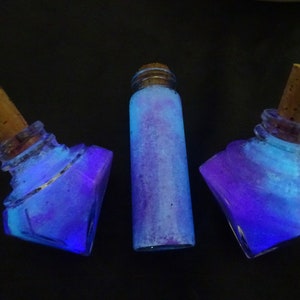 May include: Three glass bottles with cork stoppers filled with a blue and purple glittery liquid. The bottles are on a black background.