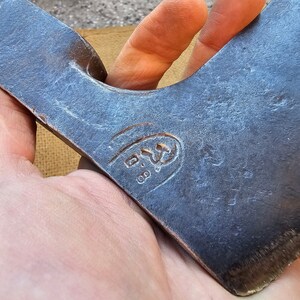 Op de afbeelding: Close-up van een blauwe stalen bijlkop met een gestempelde markering die "B.S. 08" luidt.