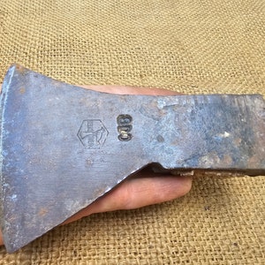 Pode incluir: Uma cabeça de machado vintage com um cabo de metal. A cabeça do machado é feita de aço e tem um acabamento preto. A cabeça do machado tem um logotipo hexagonal com o texto "E.L.M.W.E.R.C." e o número "600" estampado nele.