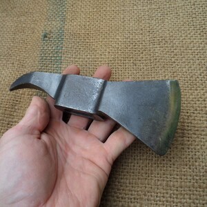 May include: A vintage, hand-forged axe with a curved blade and a wooden handle. The axe is made of metal and has a rustic, weathered look.