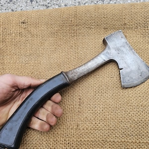 以下が含まれることがあります： 黒い柄と金属製のヘッドを持つヴィンテージの斧。斧はわずかに湾曲した刃と木製の柄を持っています。