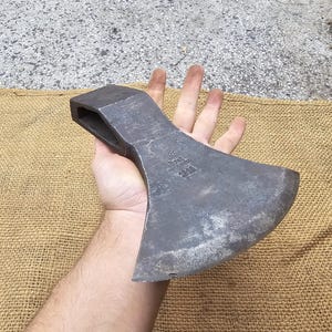 Könnte beinhalten: Eine große, robuste Axt mit einem schwarzen Metallkopf und einem Holzstiel. Die Axt hat eine scharfe Klinge und einen abgerundeten Kopf. Die Axt ist aus hochwertigen Materialien gefertigt und perfekt zum Holzhacken.
