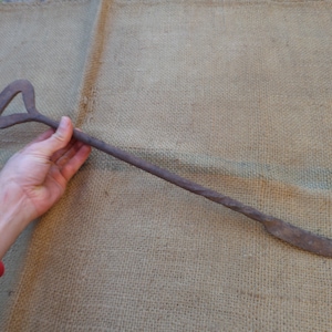 Könnte beinhalten: Ein rostiger Haken aus Metall mit einem gedrehten Griff und einem gebogenen Ende. Der Haken ist etwa 60 cm lang.