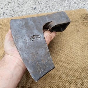 Pode incluir: Um machado vintage forjado à mão com uma cabeça de aço e um cabo de madeira. A cabeça do machado tem uma marca estampada que diz "JHT 1900".
