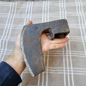 以下が含まれることがあります： 曲がった刃と木製の柄が付いた、ヴィンテージの頑丈な肉切り包丁。 金属製の刃は、使用感と経年劣化を示しており、暗く風化した外観です。 肉切り包丁は手で持たれており、そのサイズとデザインを示しています。