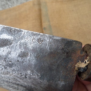 Puede incluir: Primer plano de un cuchillo de metal oxidado con mango de madera. La hoja tiene la inscripción "K & R".
