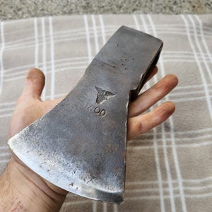 以下が含まれることがあります： 使い古された金属仕上げのヴィンテージの斧頭。 斧頭には刻印されたエンブレムと数字「1400」があります。 斧頭は手で持たれており、そのサイズとデザインを示しています。 これはツールです。