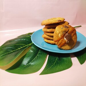 Può includere: Un mucchio di biscotti al cioccolato con gocce di cioccolato con caramello gocciolante sopra, su un piatto blu con uno sfondo di foglie verdi.