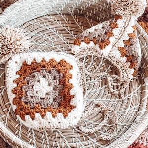 May include: Two crocheted hats with pom-poms in a natural woven basket. The hats are in shades of brown, beige, and white.