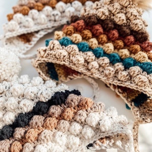 Puede incluir: Tres gorros de ganchillo con un patr&oacute;n de punto bobble. Los gorros est&aacute;n en diferentes combinaciones de colores, incluyendo marr&oacute;n, beige, azul verdoso, negro y blanco.