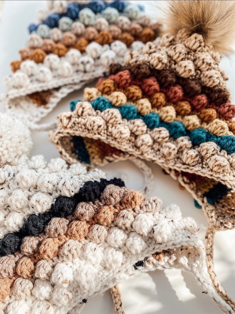 Puede incluir: Tres gorros de ganchillo con un patr&oacute;n de punto bobble. Los gorros est&aacute;n en diferentes combinaciones de colores, incluyendo marr&oacute;n, beige, azul verdoso, negro y blanco.