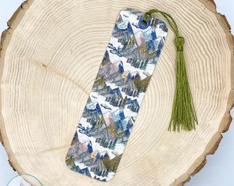 May include: A white bookmark with a colorful mountain landscape design and a green tassel. The bookmark is made of durable material and is perfect for marking your place in a book.