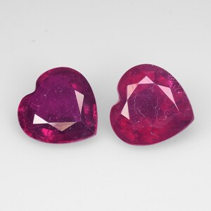 May include: Two heart-shaped ruby gemstones, each with a deep red colour and a faceted cut.