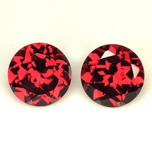 May include: Two round, red gemstones with a faceted cut. The gemstones are set against a white background.