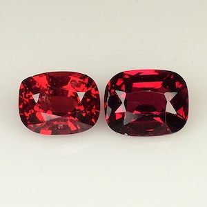 Peut inclure: Deux pierres précieuses rouges, taillées en forme de coussin, sont présentées sur un fond blanc. Les pierres précieuses sont à peu près de la même taille et ont une teinte rouge similaire.