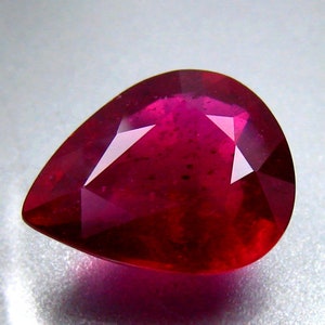 May include: A deep red pear-shaped gemstone with a faceted cut. The gemstone is set against a white background.