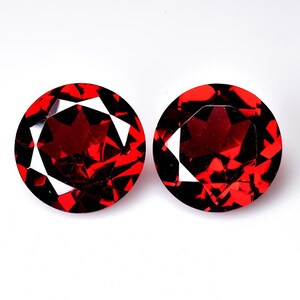 May include: Two round, red gemstones with a faceted cut. The gemstones are set in a clear, round setting.