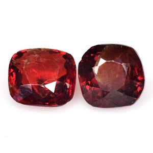 Puede incluir: Dos gemas facetadas, talladas en cojín. Las gemas son de color rojo intenso con inclusiones internas y un alto grado de transparencia. Las facetas reflejan la luz, creando un efecto brillante. Las gemas se presentan sobre un fondo blanco.