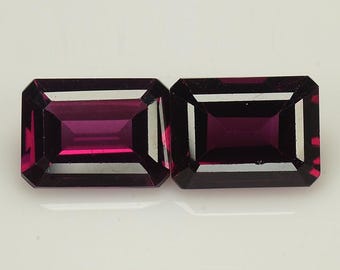 May include: Two rectangular, faceted gemstones with a deep purple hue. The gemstones are cut in a step-cut style, with a polished finish.