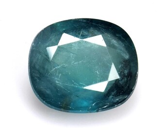 May include: A faceted, oval-shaped gemstone with a teal and blue color gradient. The gem has a polished surface with internal inclusions and a star-like pattern in the center. The gemstone is set against a white background.