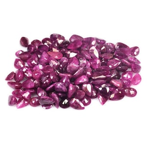 May include: A large pile of loose pear-shaped ruby gemstones. The rubies are a deep pink color and have a faceted cut.