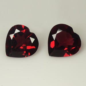 May include: Two heart-shaped red gemstones with a faceted cut.