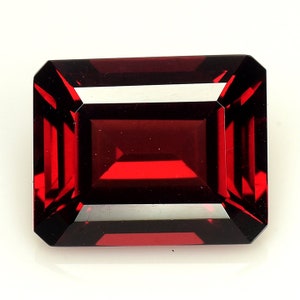 May include: A deep red gemstone with a rectangular emerald cut. The gemstone is faceted and has a high polish.
