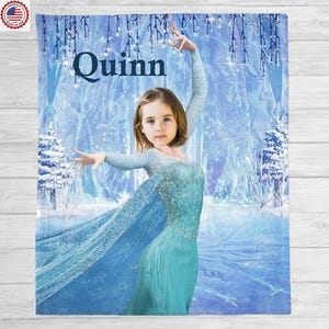 May include: A personalized blue blanket featuring a young girl in a teal dress, set against a winter wonderland backdrop. The name "Quinn" is displayed in large, dark blue letters at the top. The blanket has a soft, plush appearance.