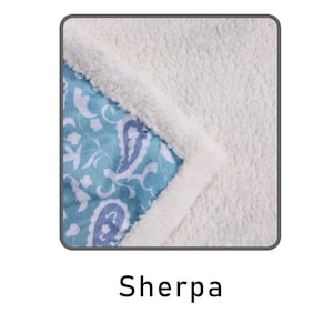 May include: Close-up of three different types of blanket fabric: fleece, sherpa, and mink. The fleece fabric is a soft, blue and white floral print. The sherpa fabric is a white, fluffy material. The mink fabric is a white, plush material.