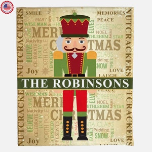 May include: A festive Christmas themed throw blanket featuring a Nutcracker illustration surrounded by words like "Merry Christmas", "Joy", "Love", "Peace", and "Nativity". The blanket is personalized with the name "The Robinsons".